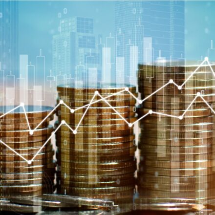 Image of coins stacked in various heights with a charts digitally overlaid to show performance of financial metrics against a sky blue background.