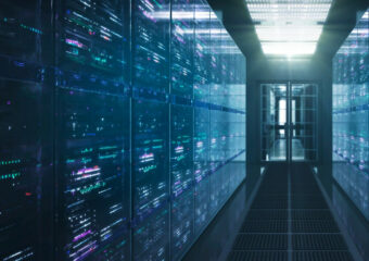 Row of servers inside closed section of data center, with view from hallway towards door in the background.