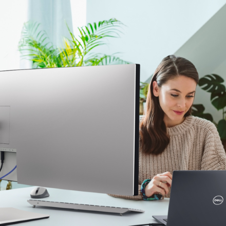 Woman working remotely using a Dell UltraSharp 49 Curved USB-C Hub Monitor and a Dell Latitude 5000 series model laptop.