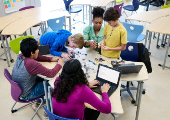 Teacher is working with elementary school age children in a small group class activity using Dell Latitude 3120 notebooks.