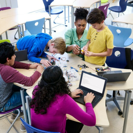 Teacher is working with elementary school age children in a small group class activity using Dell Latitude 3120 notebooks.