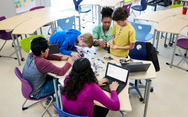 Teacher is working with elementary school age children in a small group class activity using Dell Latitude 3120 notebooks.