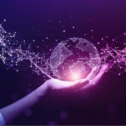 Digital image of a globe made of information code with new data moving through it, held by a woman's hand, against a purple background.