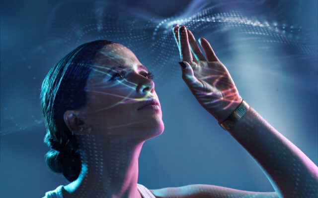 Young Caucausian woman holds her left hand up as high tech effects appear around her fingers and reflect on her face.