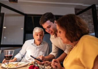 Explaining AI to Grandma. Grandchild showing something on the mobile phone to his grandparents at Christmas dinner