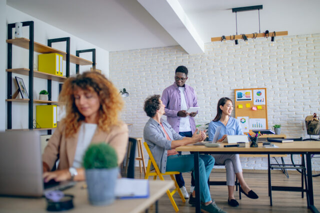 Businesswoman using laptop at modern office, her colleagues are working in the background