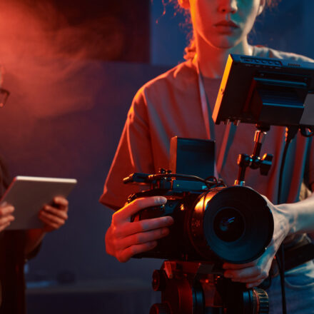 Cropped shot of female cameraman operating equipment in studio set with neon lights copy space